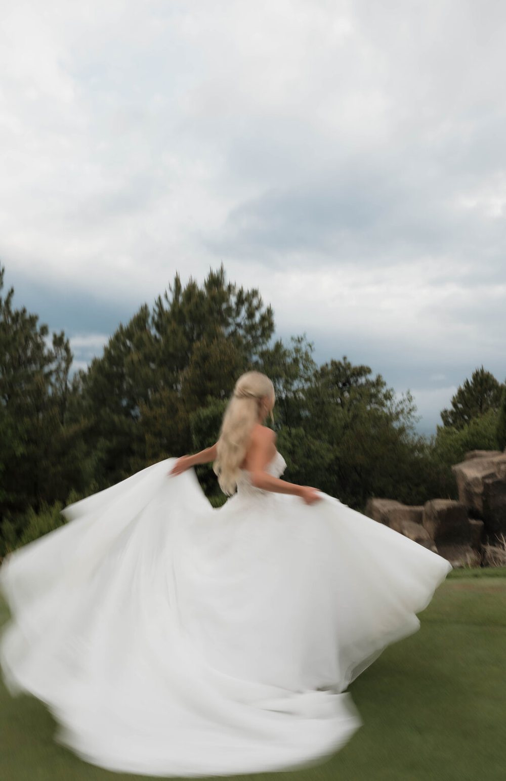 A bride spinning in her gown on a hillside lawn, hair swept half up and flying with the turn