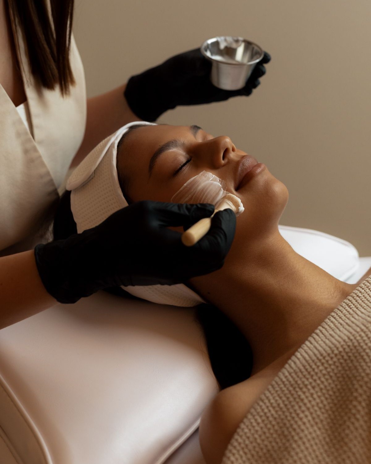 An esthetician applying a facial treatment in a warm studio, the service an esthetician website has to explain and book
