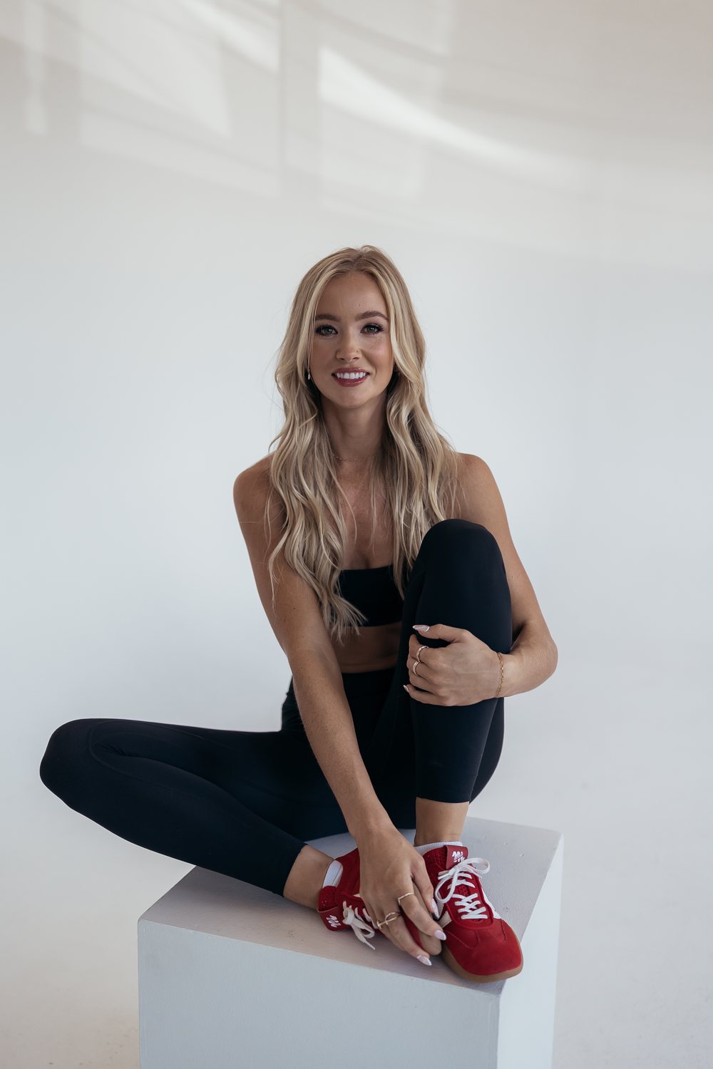 Sabrina of Salt and Sage Studios seated on a white block in a black Pilates set, one knee pulled in, smiling at the camera